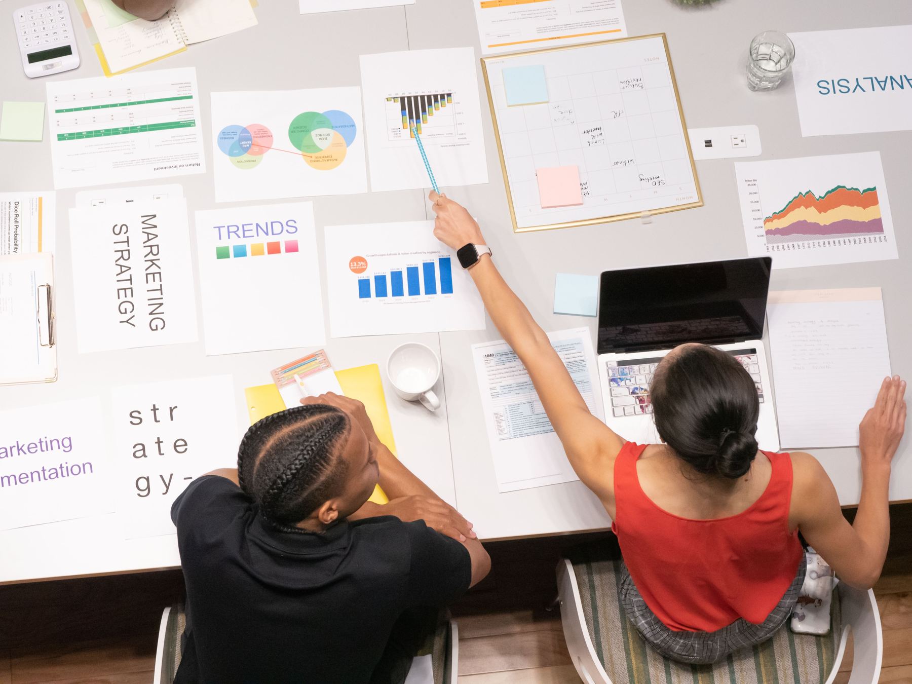 Two colleagues reaching across a table of printed reports to point at a bar chart